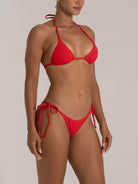 Side-angle view of a woman in a red halter triangle bikini set with adjustable tie sides.