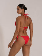 Woman in a red textured triangle bikini with side-tie bottoms, back view.
