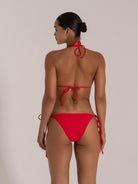 Woman wearing a red triangle bikini with halter neck and string tie back, back view.