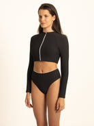 Close-up of the Ocean Mystery ribbed black rash guard crop top with the front zipper partially open, highlighting the premium fabric texture and elegant white piping detail.