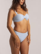 Side view of a woman in a light blue ribbed bikini with twist detail and supportive wide straps.