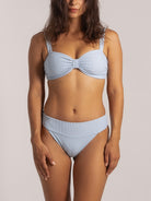 Woman wearing a ribbed light blue bikini set with twist front top and high-waisted bottom, front view.