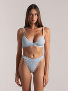 Front full body view of woman in light blue ribbed bikini top and high cut bottom