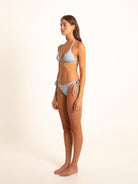 Model wearing soft blue bikini turning slightly right, showing flattering side shape