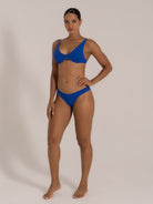 Side pose of model in a royal blue bikini with a scoop neckline and mid-rise bikini bottoms.