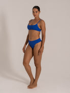 Model side posing in royal blue textured bikini set with scoop neckline and wide waistband bottom.