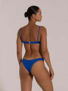 Woman wearing royal blue bikini with underwire top and full coverage bottom, back view