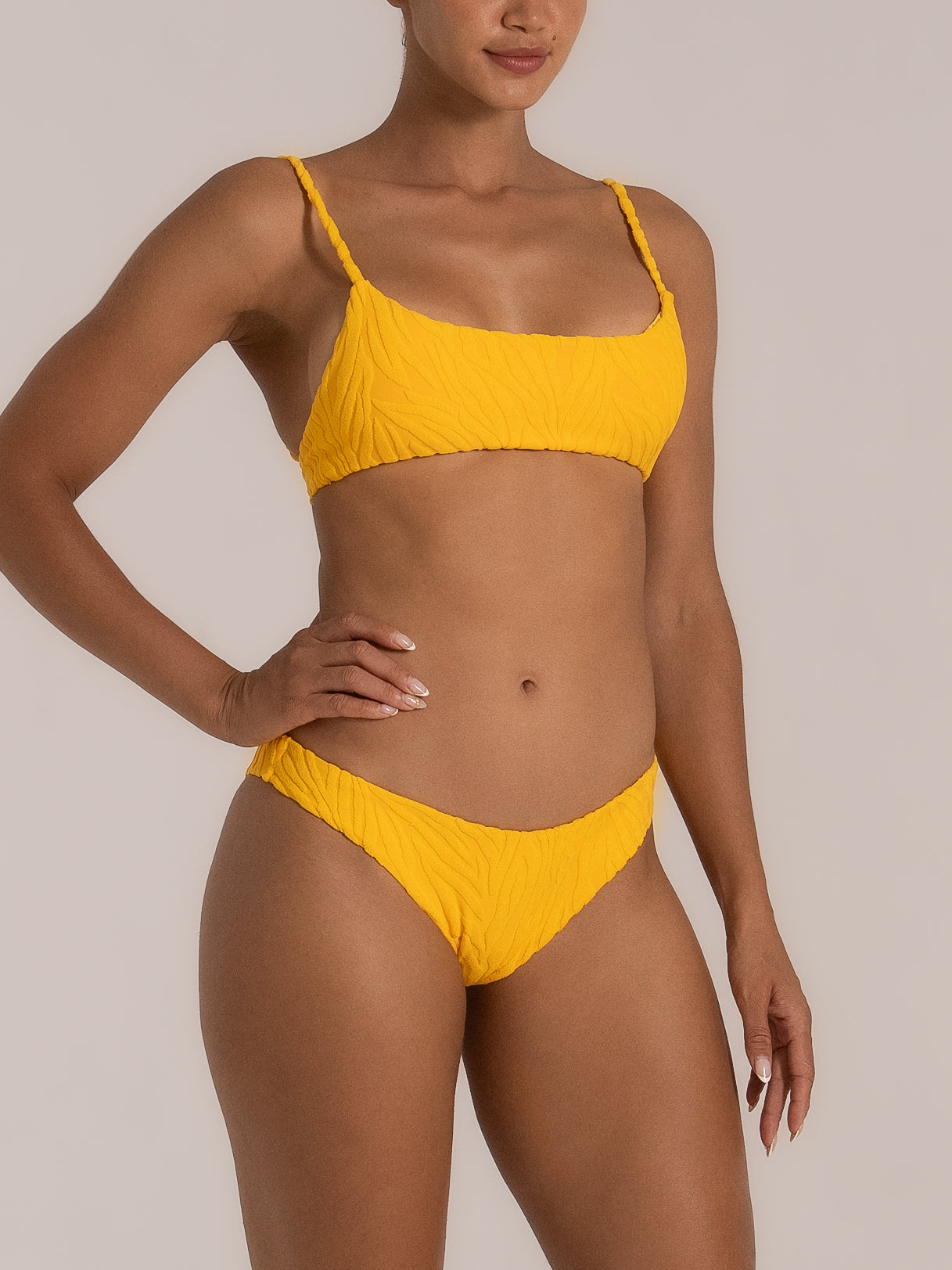 Side profile of a scoop-cut yellow bikini bottom in stretch textured material.