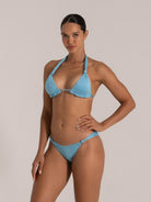 Side front view of a woman in a baby blue shimmer bikini with halter neck and ruched triangle top.