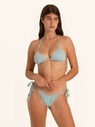 Lifestyle shot of woman in shimmer light blue tie side bikini bottom with relaxed pose.