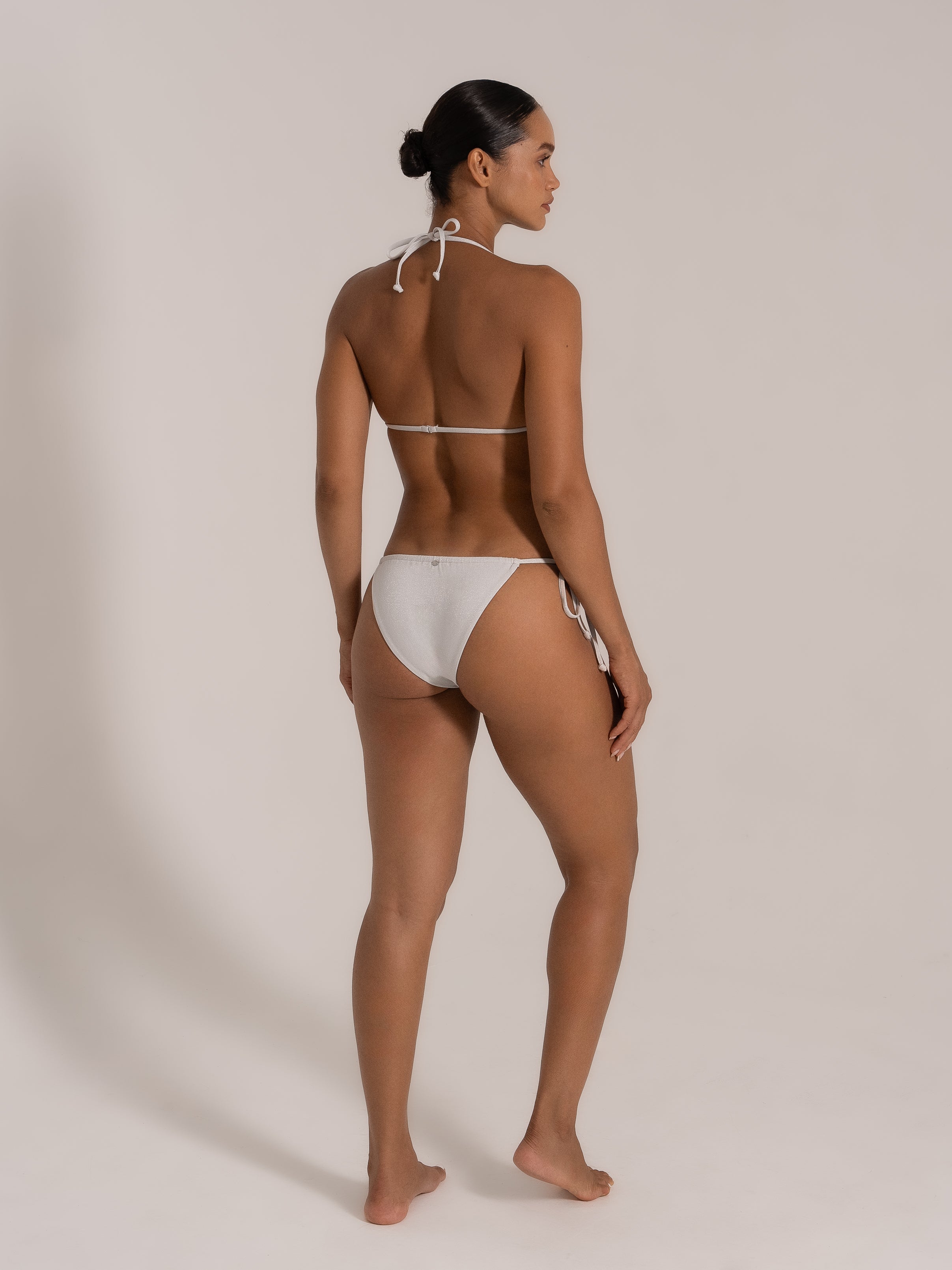Side-back view of white glitter triangle bikini with side tie bottoms and thin back straps.
