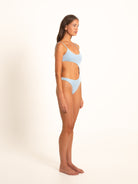 Side profile of woman in asymmetric cut-out blue one-piece swimsuit with ring detail