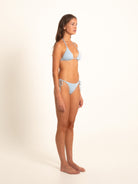 Woman in textured blue triangle bikini, shown in relaxed side profile pose