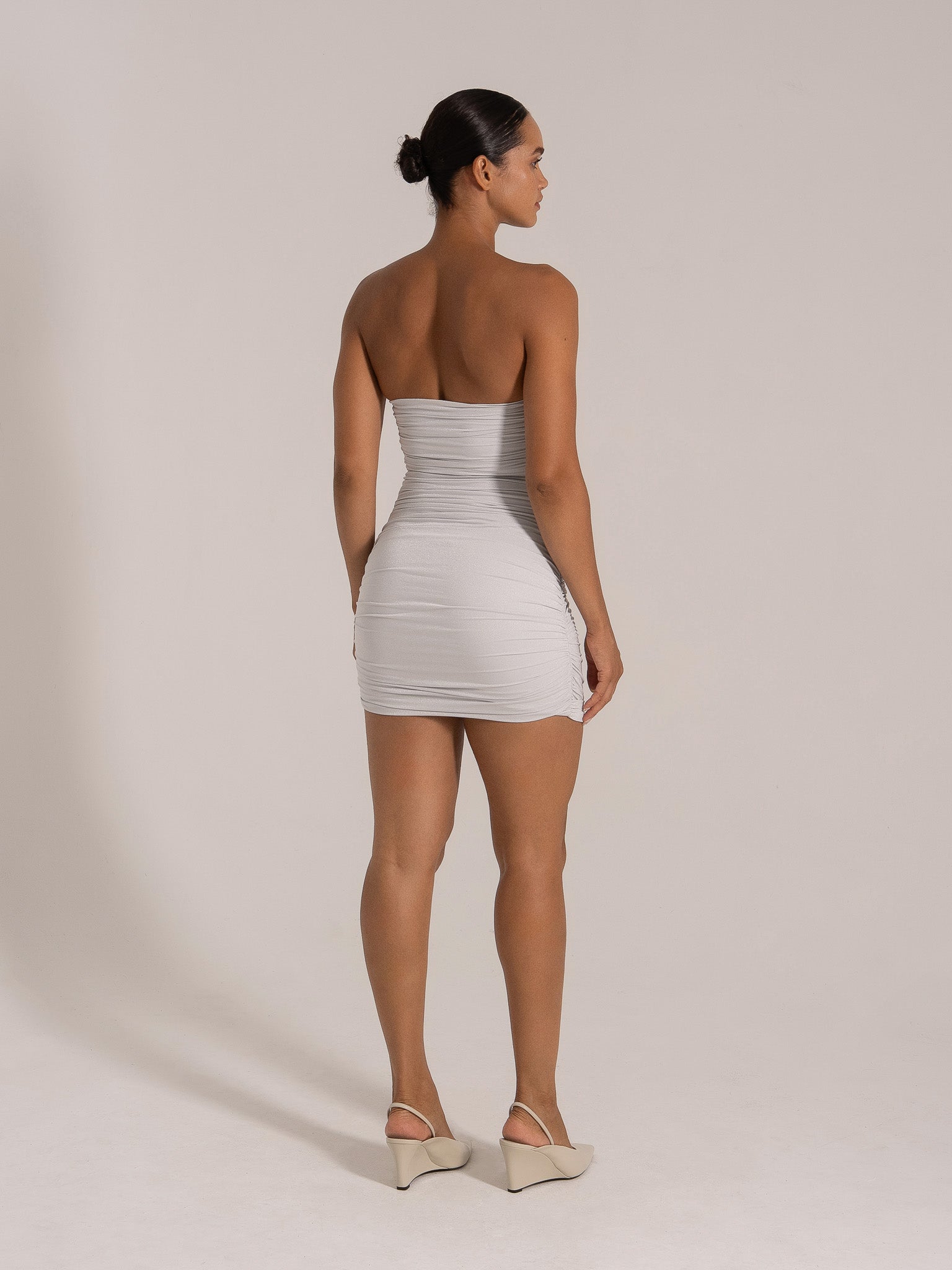 Side view of a woman in a fitted silver strapless dress with ruched details