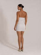 Woman wearing a silver strapless ruched mini dress with a back slit