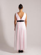 Rear view of a formal maxi dress in pink and white tones featuring a plunging V-back and a cinched black waistband.