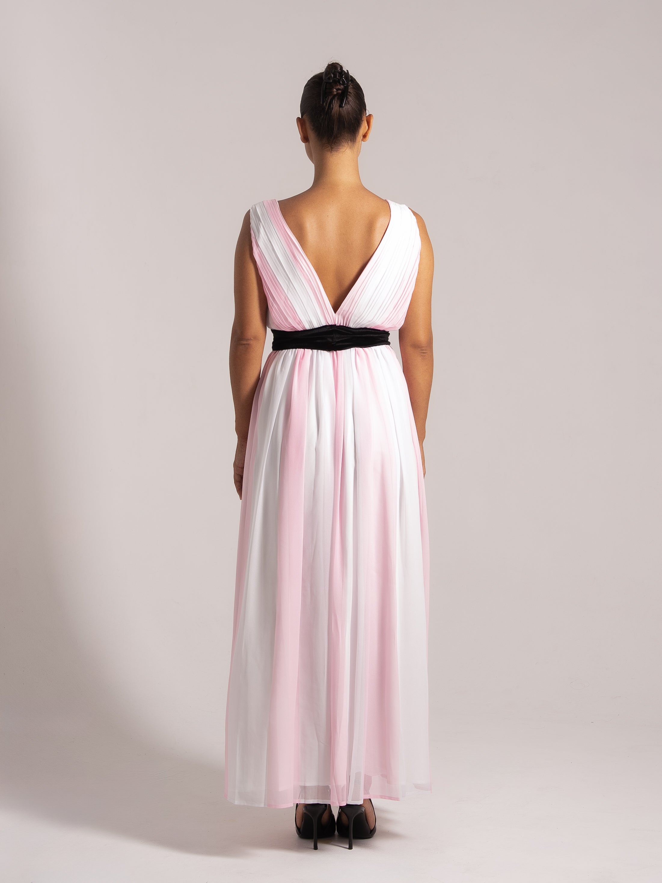Rear view of a formal maxi dress in pink and white tones featuring a plunging V-back and a cinched black waistband.