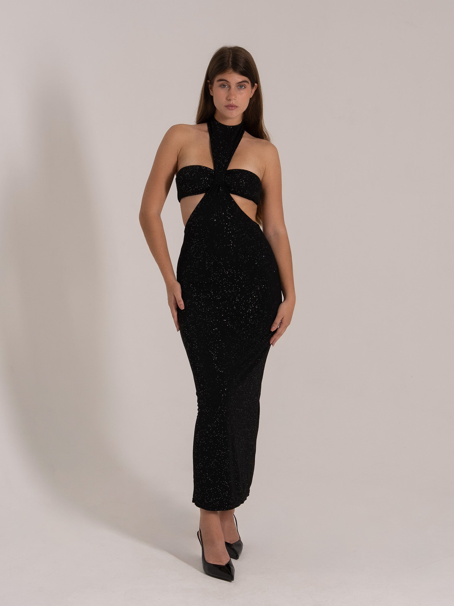 Front view of a woman in a black sparkle maxi dress featuring a halter neck, cutout bodice, and elegant silhouette.