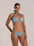 Woman modeling a glittery baby blue bikini set with halter neck, ruched bikini top, and knotted sides.