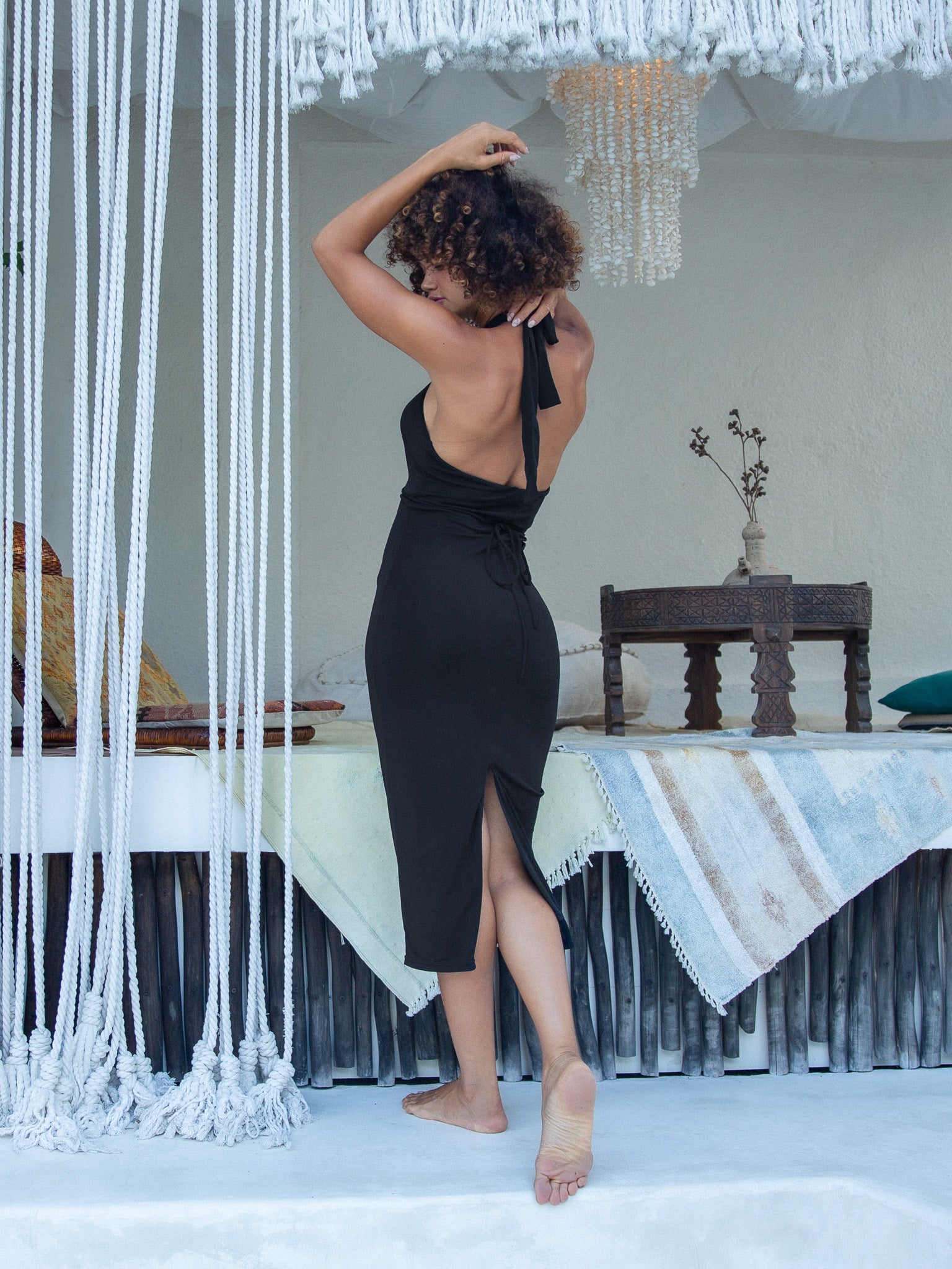 Stylish woman in a black mid-length dress with a crisscross halter style, chest cut-out with intersecting woven straps, open back design, and a slit detail on dual-layer material.