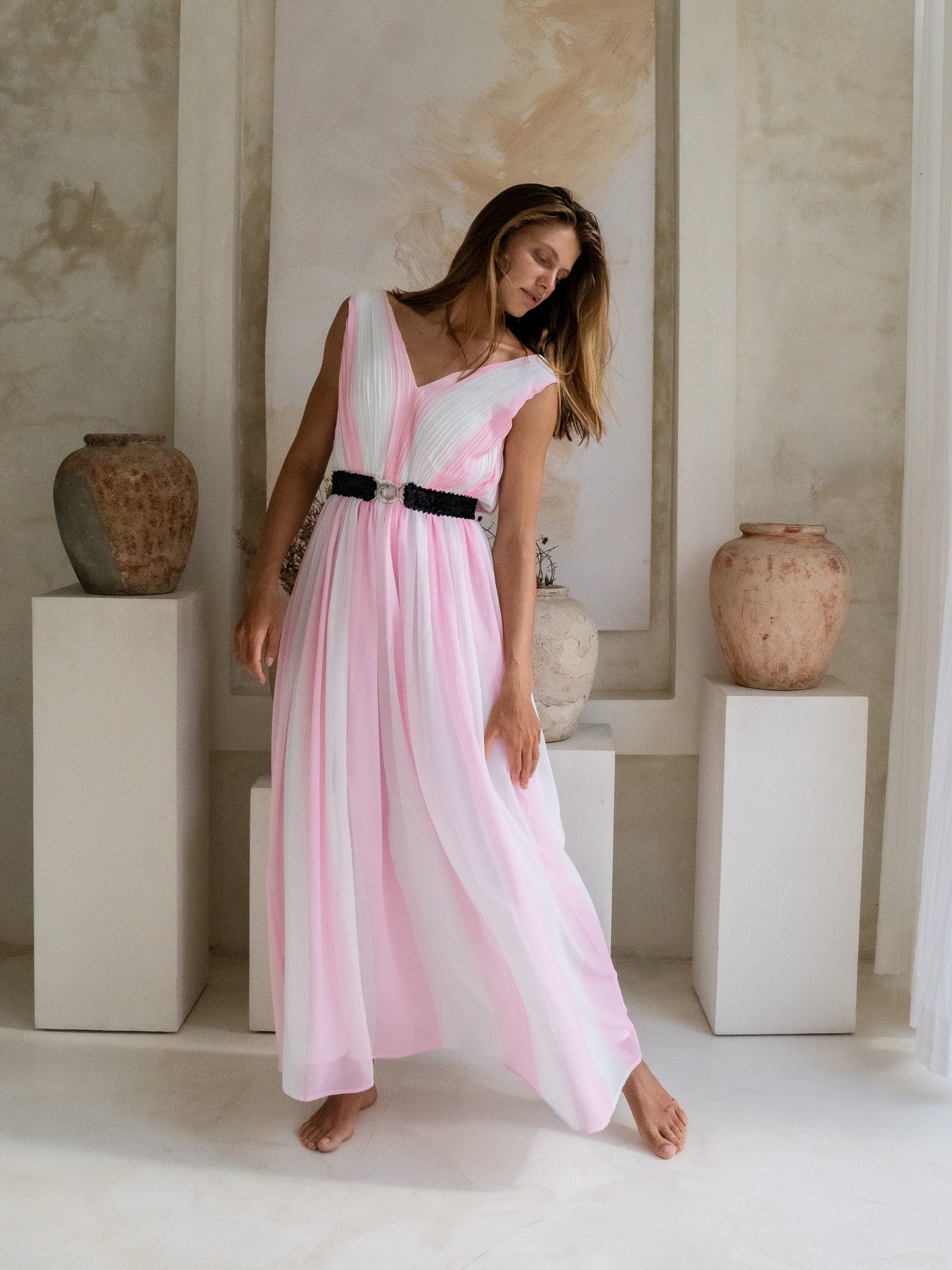 Stylish woman in a white and pink pleated maxi dress with a flattering V-neck and chic black sequin waistband.