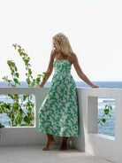 Stylish woman in a green floral dress with spaghetti straps on a beachfront villa balcony