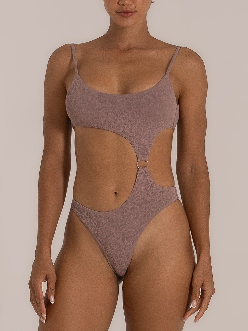 Front view of a woman wearing a taupe one-piece swimsuit featuring side cutouts and a gold ring detail at the waist, combining sleek minimalism with a modern silhouette.
