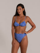 Model poses in a textured blue two-piece bikini with ruched fabric and a central ring accent, perfect for beachwear.