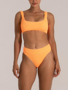 Woman in a bright orange bikini with a square neckline and thick straps, high-waisted bottom, front view.