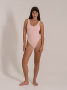Front-facing view of a woman in a textured light pink one-piece swimsuit with a rounded neckline and high-cut legs