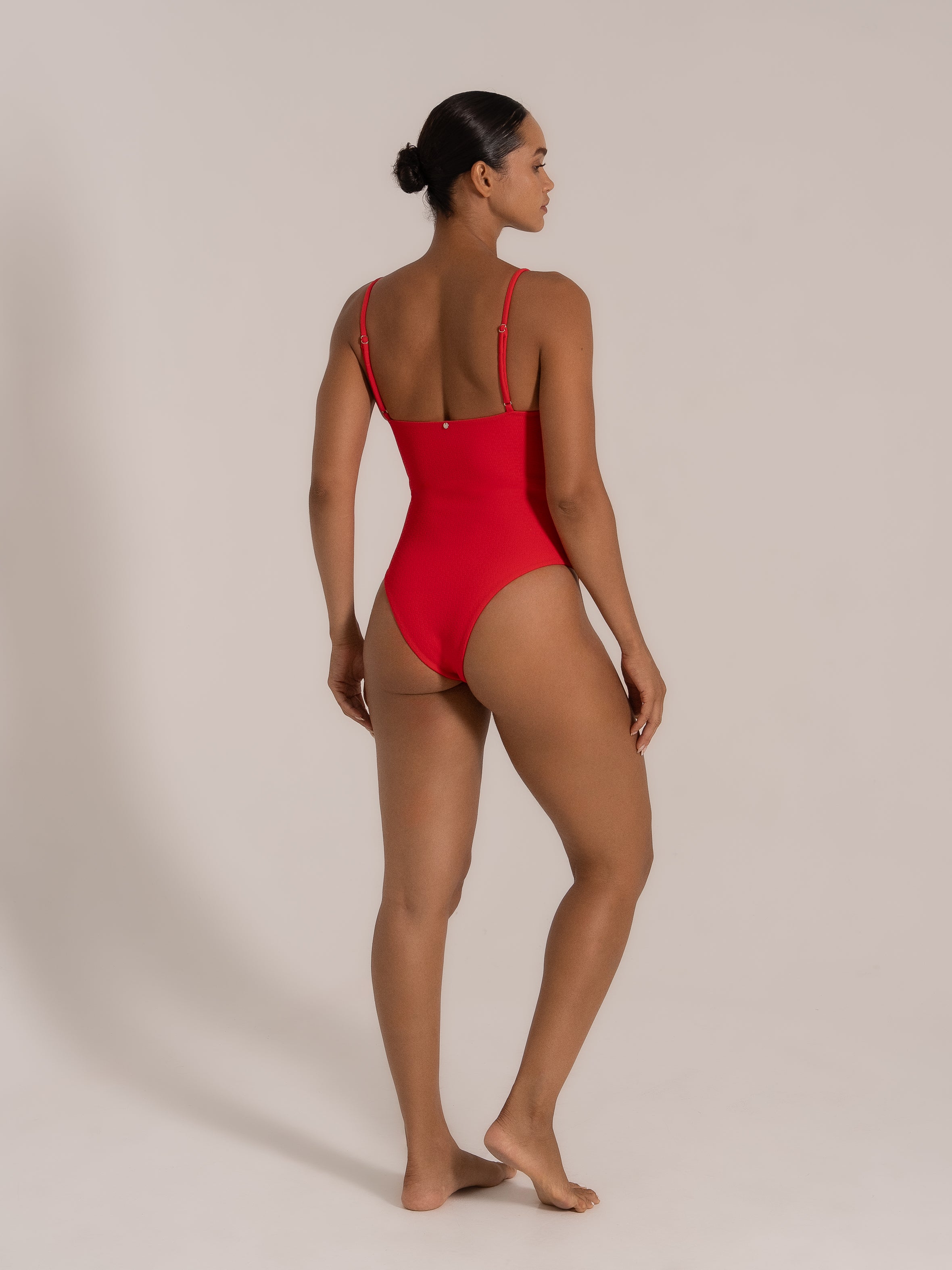 Model wearing a red textured one-piece, side-back angle with square-cut back.