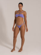 Model in twist front purple bandeau bikini with cheeky bottoms, angled pose