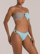 Woman wearing a two-tone bandeau bikini top in blue and grey with wooden ring detail at the front, styled for a chic beach look