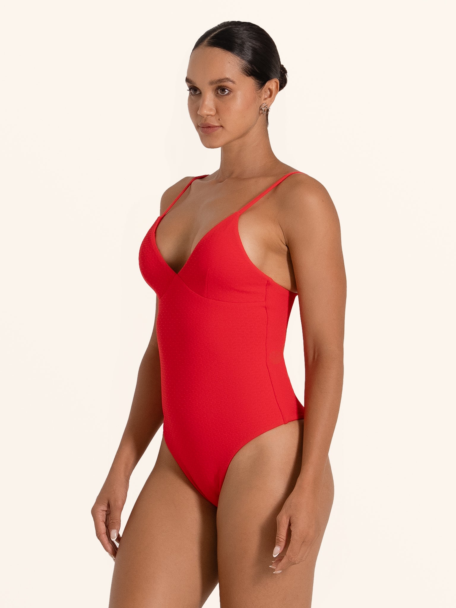 Side front pose of woman wearing red one piece swimsuit with V neckline and sleek fit.