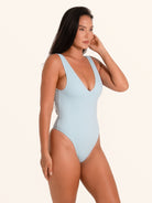 Side pose of woman in baby blue textured one piece swimsuit with V neckline and high cut leg.