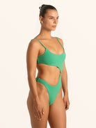 Side view of woman in green textured cut out one piece swimsuit with high leg cut.