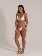 Model posing in white bikini set with slim side straps and textured detailing, perfect for a sleek beach look.