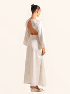 Rear side profile of white maxi dress with flared sleeves and flowing skirt