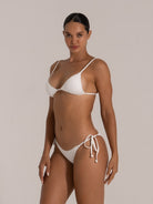 Woman modeling a white ribbed string bikini with triangle top and high-cut side tie bottom