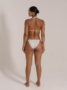 Model wearing shimmering white triangle bikini set with halter neck and back tie, back view.