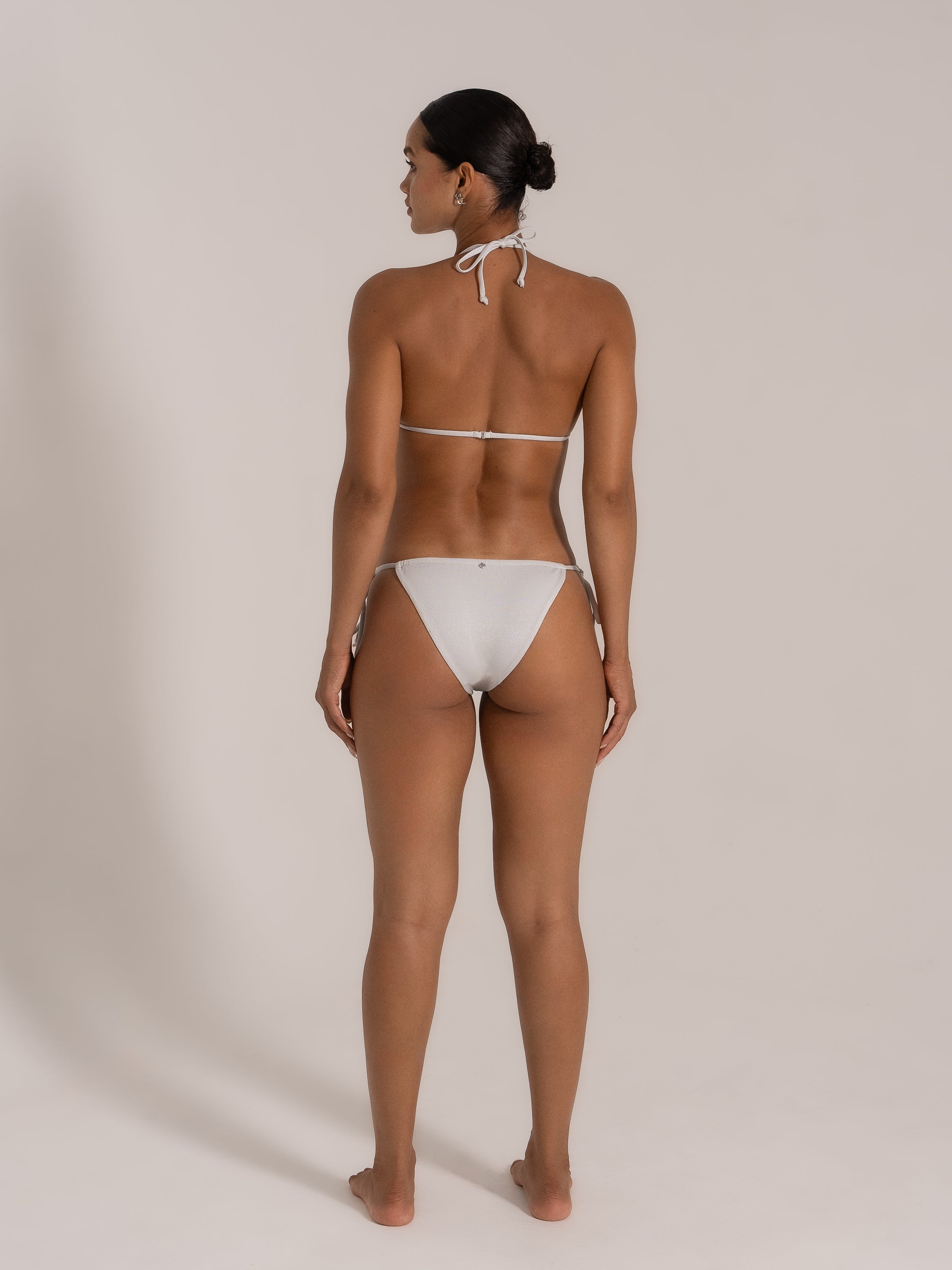 Model wearing shimmering white triangle bikini set with halter neck and back tie, back view.