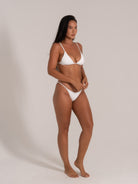 Model in white textured triangle bikini, angled side pose highlighting plunging neckline and slim straps.