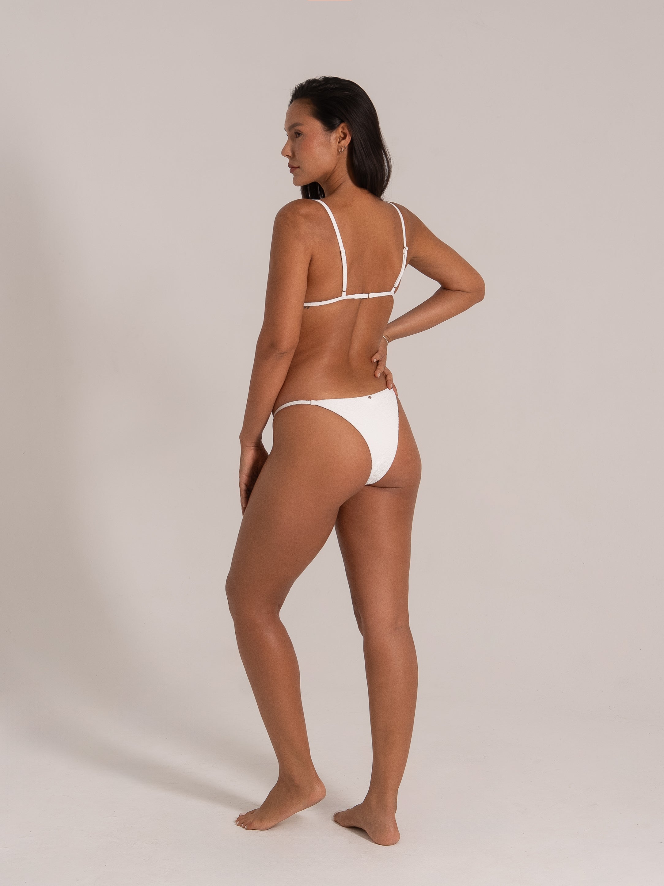 Model wearing white textured bikini set, back view showing adjustable straps and cheeky bottom fit.