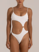 Front view of a woman wearing a white textured one-piece swimsuit featuring a scoop neckline, side cutouts, and a central gold ring detail for a sleek and contemporary beach style.
