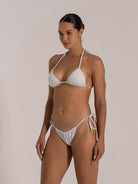 Side pose of a woman in a white shimmer triangle bikini with halter neck.