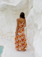 Woman in a floral spaghetti strap maxi dress standing by the water, back view.