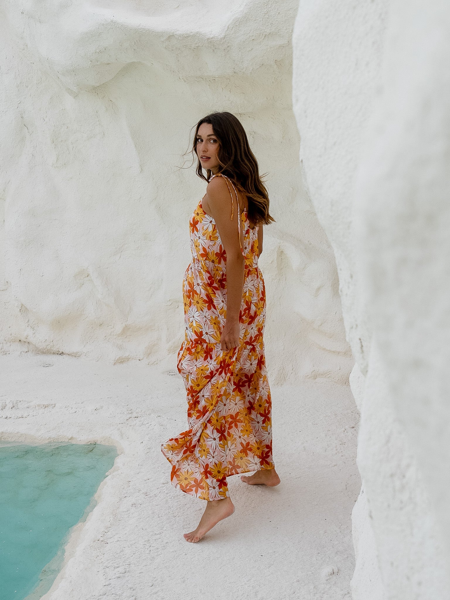 Woman in a floral spaghetti strap maxi dress standing by the water.