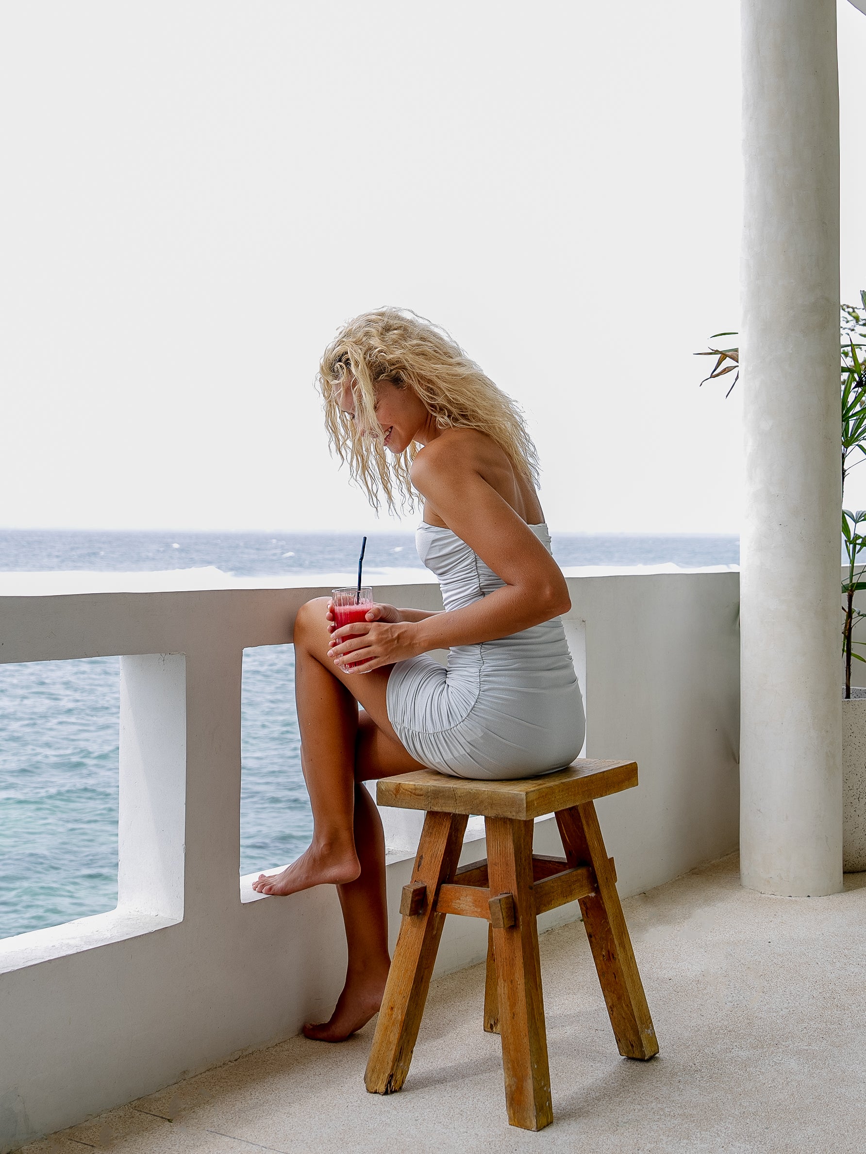 Woman wearing a shiny silver mini dress sitting on a beachside platform bench