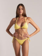 Front view of a woman wearing a yellow halter triangle bikini with side-tie bottoms.