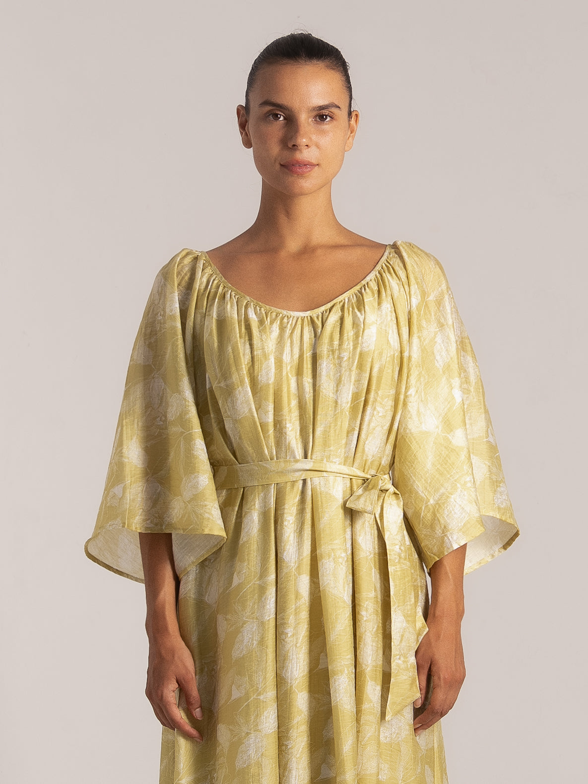 Front view of yellow midi dress with white leaf print, featuring wide sleeves, gathered neckline, and matching waist tie